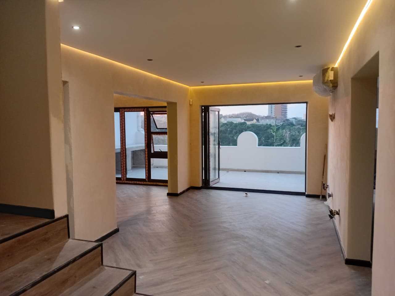 Interior painting Gqeberha — open plan lounge with warm cream walls, amber LED strip cove lighting, large sliding doors with city view beyond