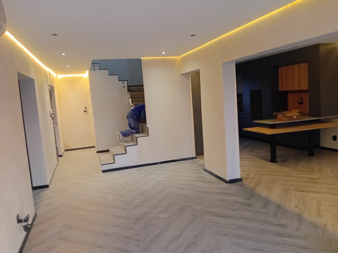 Interior painting Port Elizabeth — open plan lounge with amber LED cove lighting, white walls and columns, floating staircase and kitchen visible