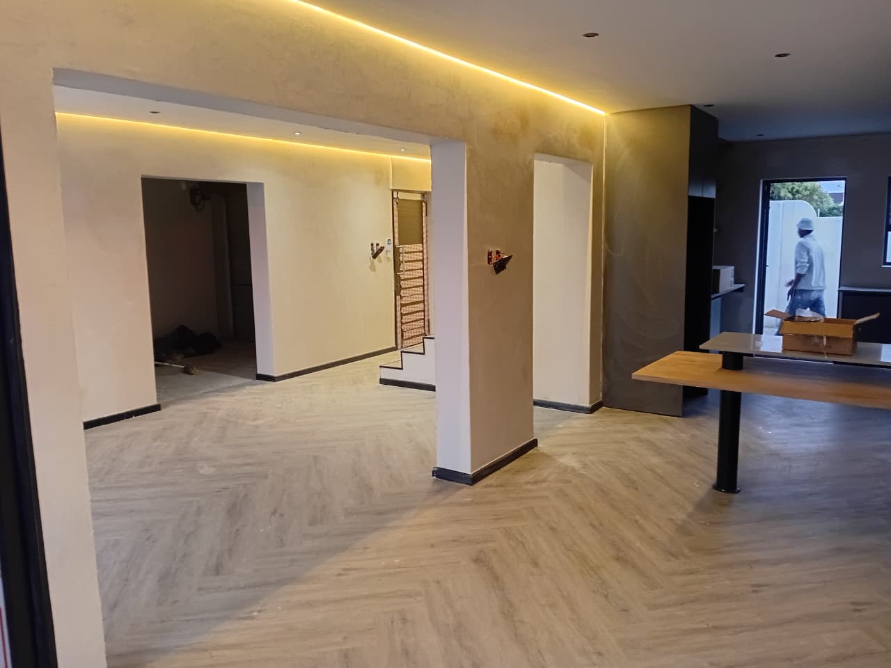 Interior painting Port Elizabeth — open plan lounge with amber LED cove, white and gold Venetian plaster walls, charcoal feature column, herringbone floor, kitchen island