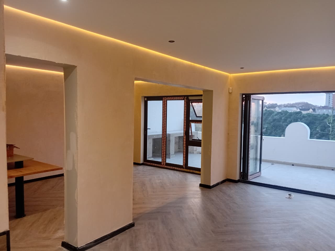 Interior painting Port Elizabeth — open plan living space with warm cream walls, amber cove lighting, folding doors and balcony view, herringbone floor