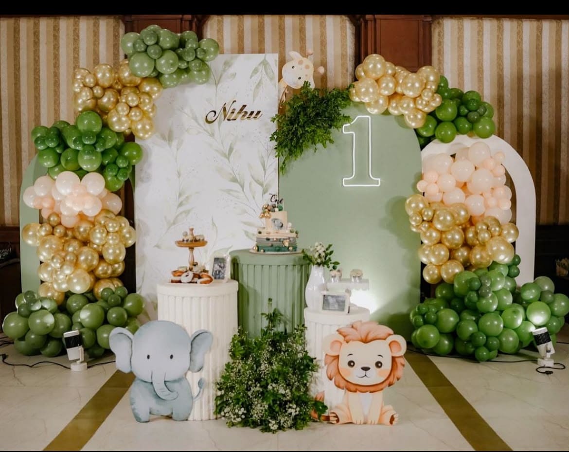 Green and gold balloon arch with animal props and a number one birthday display