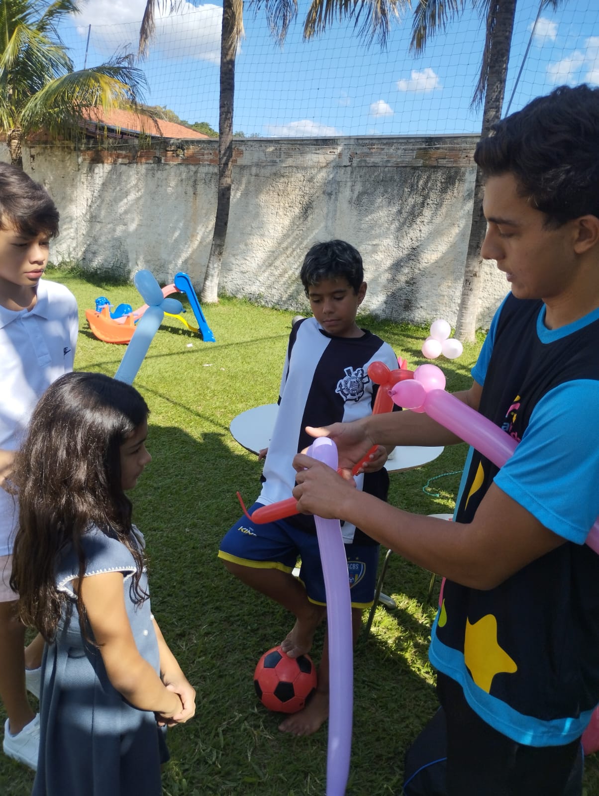 Recreador fazendo escultura de balões enquanto crianças observam no jardim