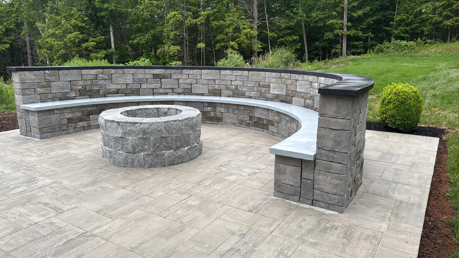 Circular stone fire pit with curved seating wall on a paved backyard patio