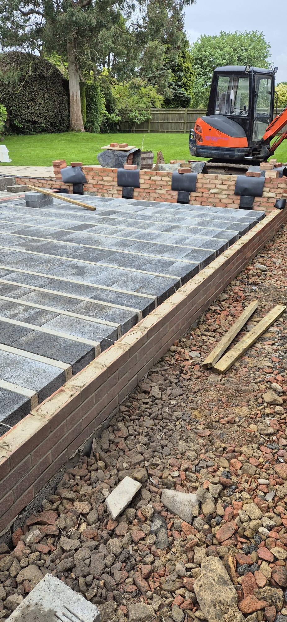 Willow Terrace & Retaining Wall — A generous split-level porcelain and stone terrace with an engineered brick retaining wall, transforming a sloping garden into usable entertaining space.
