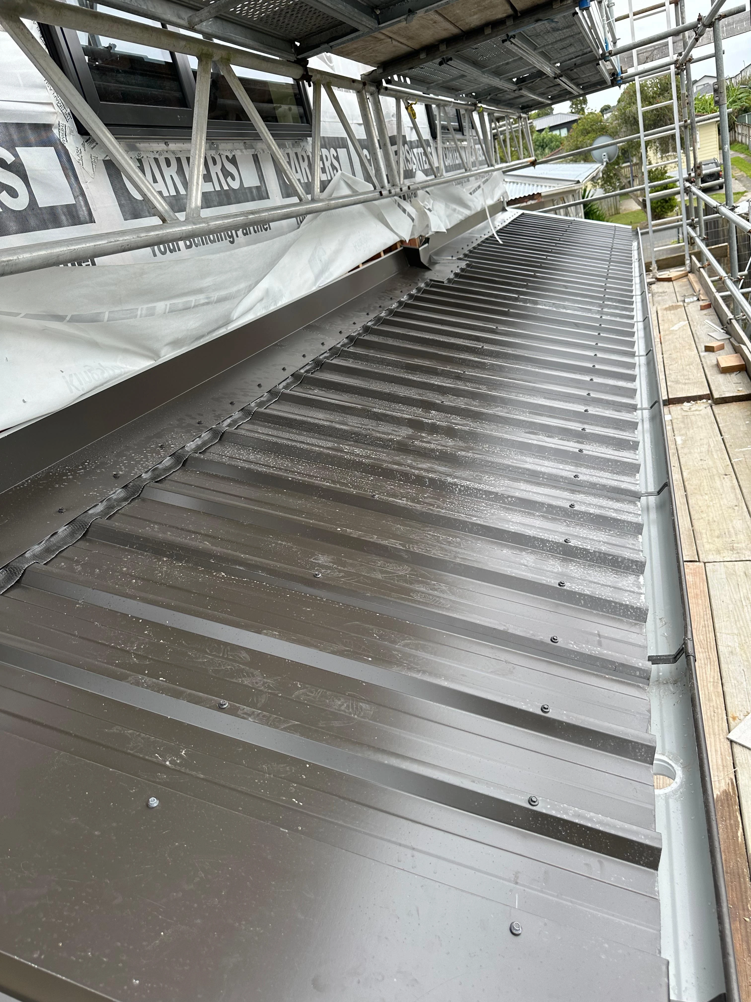 New long-run metal roof installation beside scaffolding