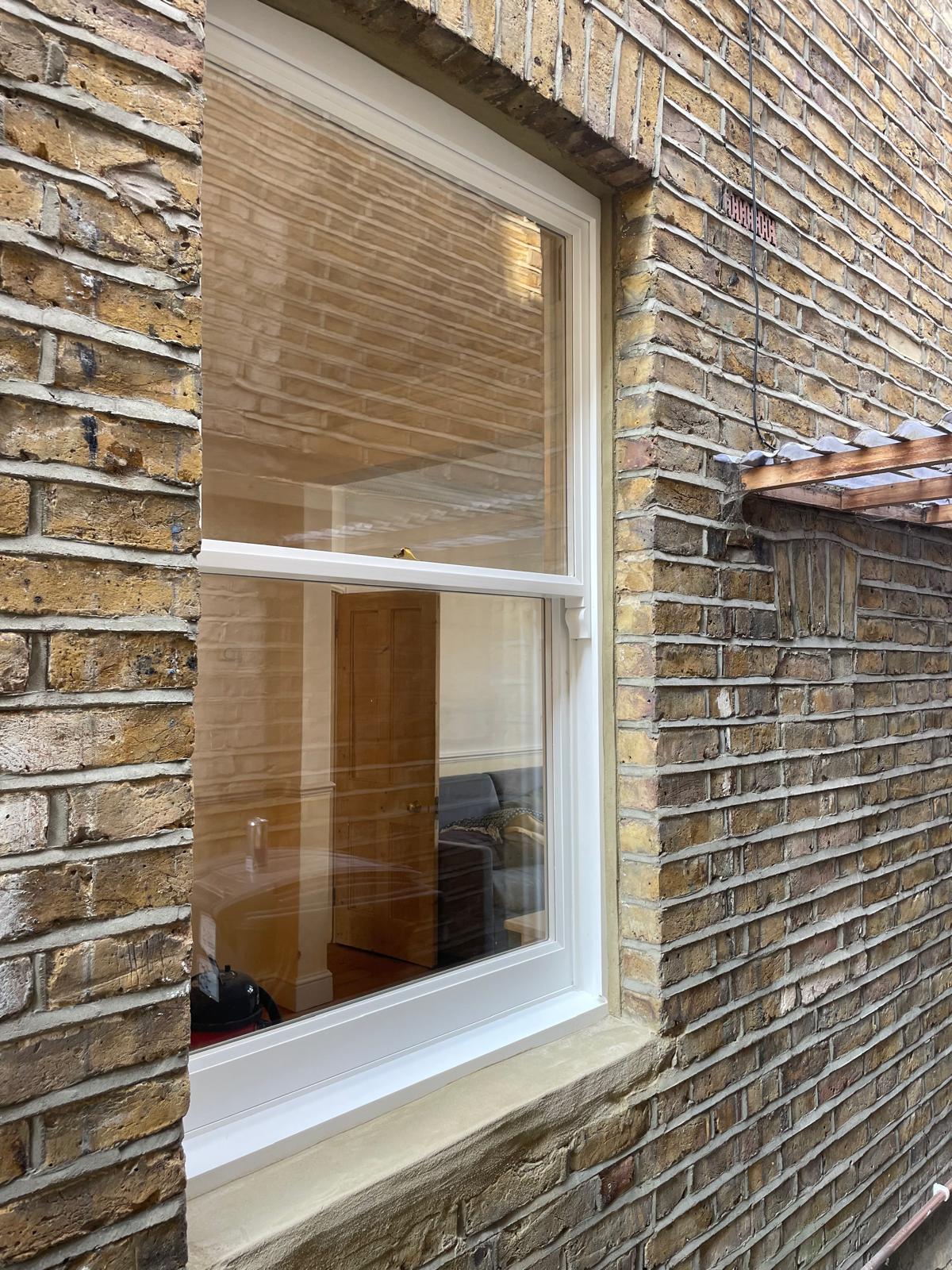 Repaired white timber sash window set into a yellow-brick wall