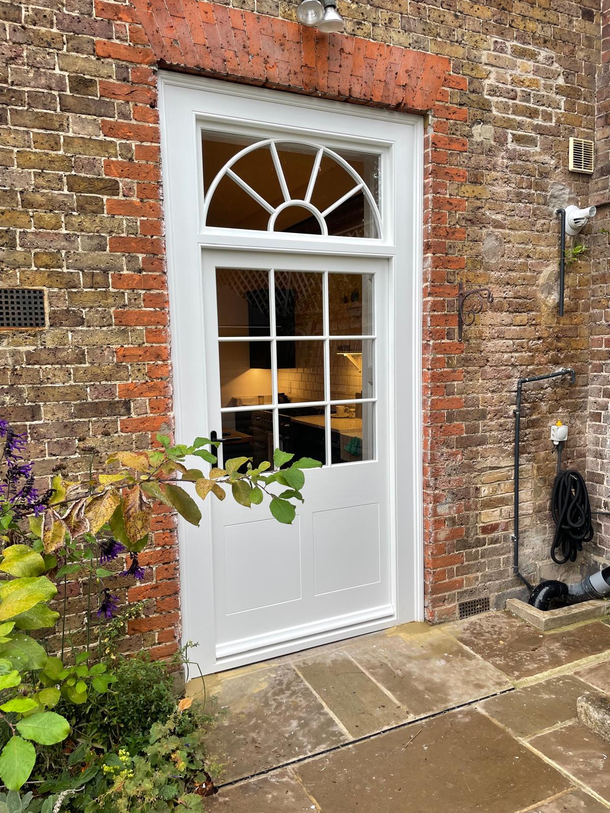 New white glazed timber door with sunburst fanlight in a brick wall