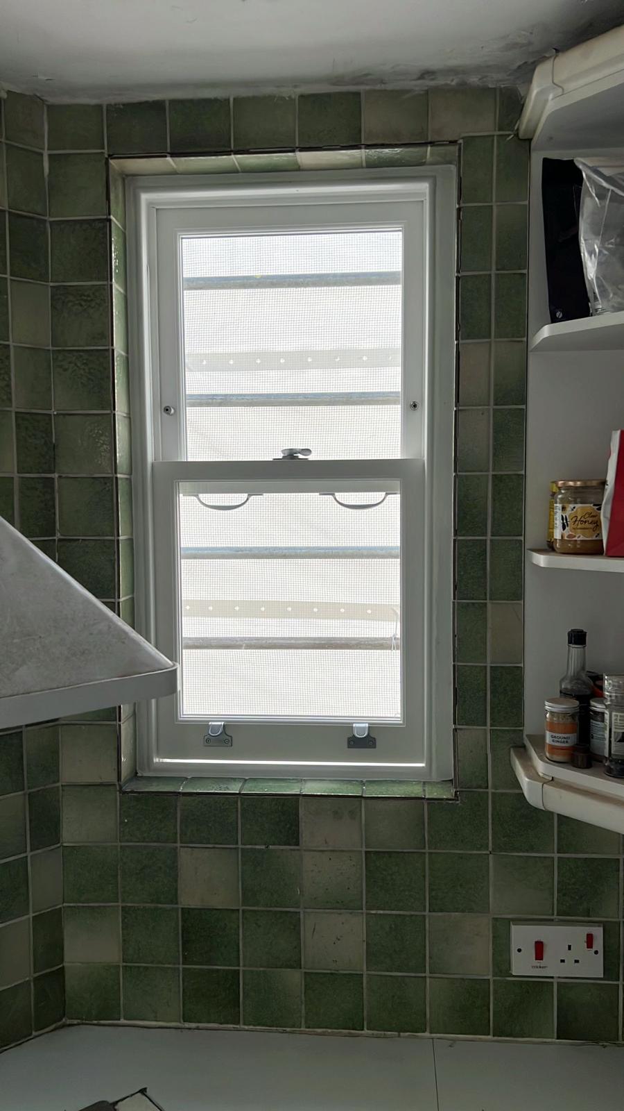 Draught-proofed white sash window in a green-tiled period kitchen