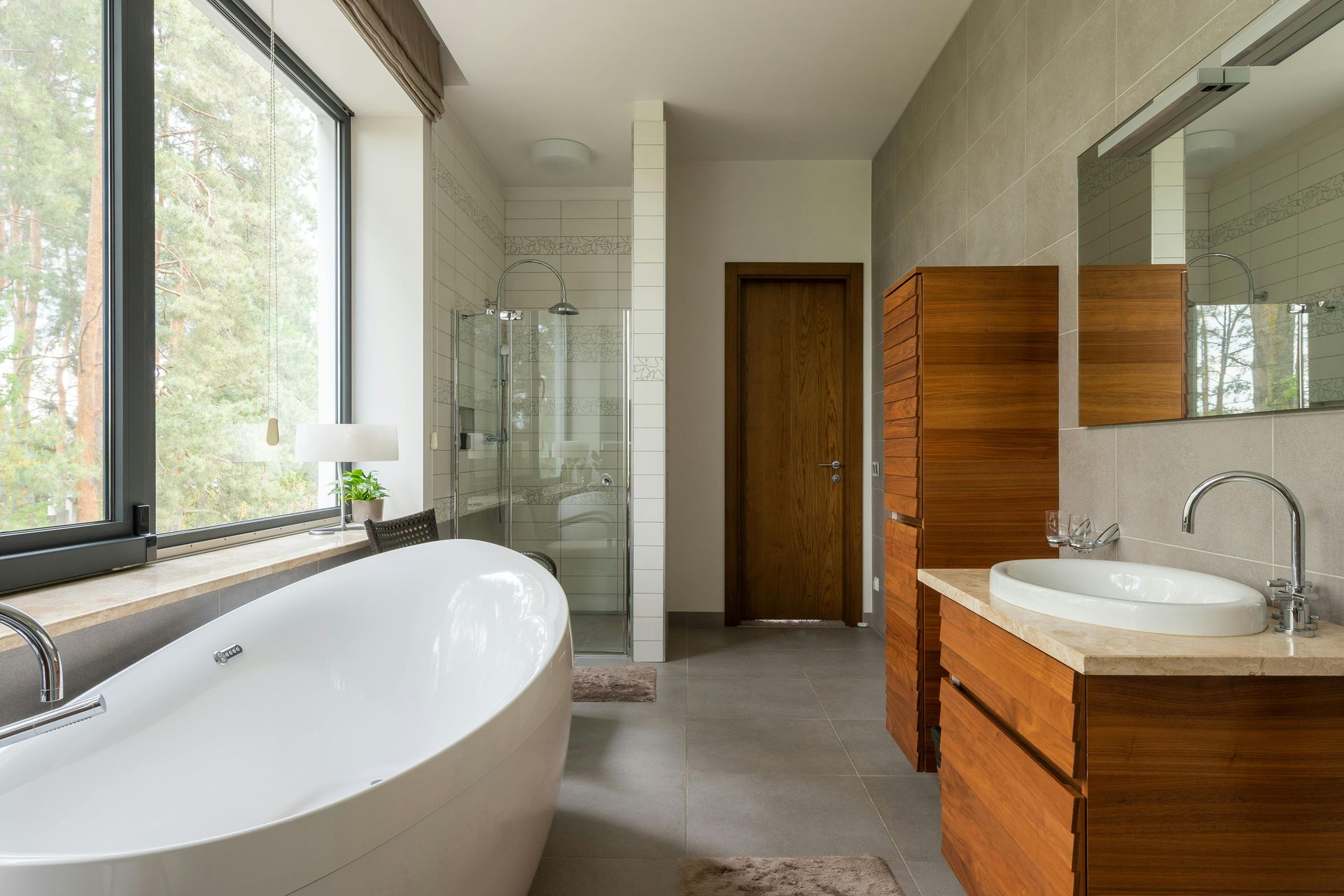 Modern remodeled bathroom with a freestanding tub by a large window, glass shower, and a warm wood vanity with a vessel sink