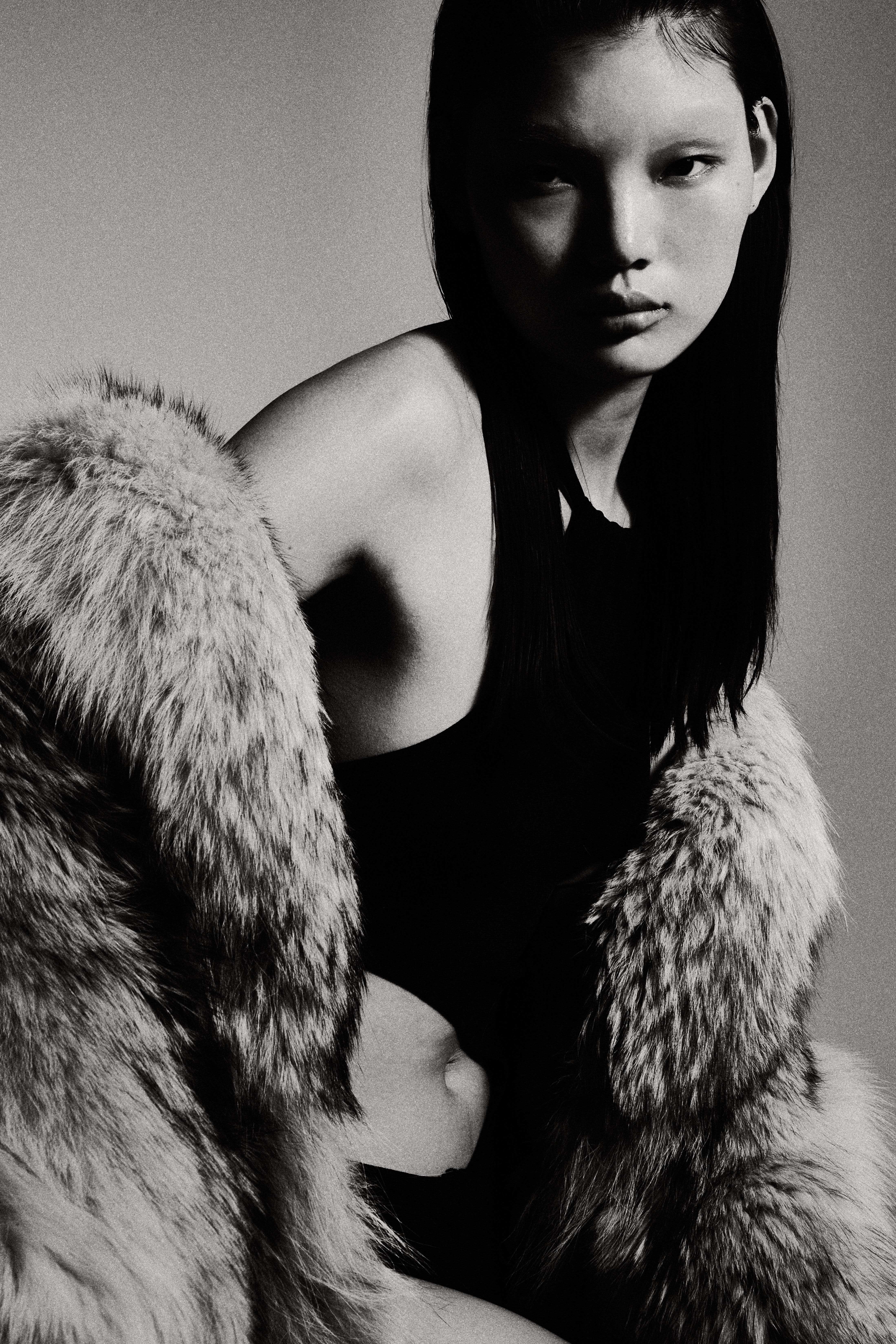 Black and white studio portrait of woman with long dark hair in fur coat