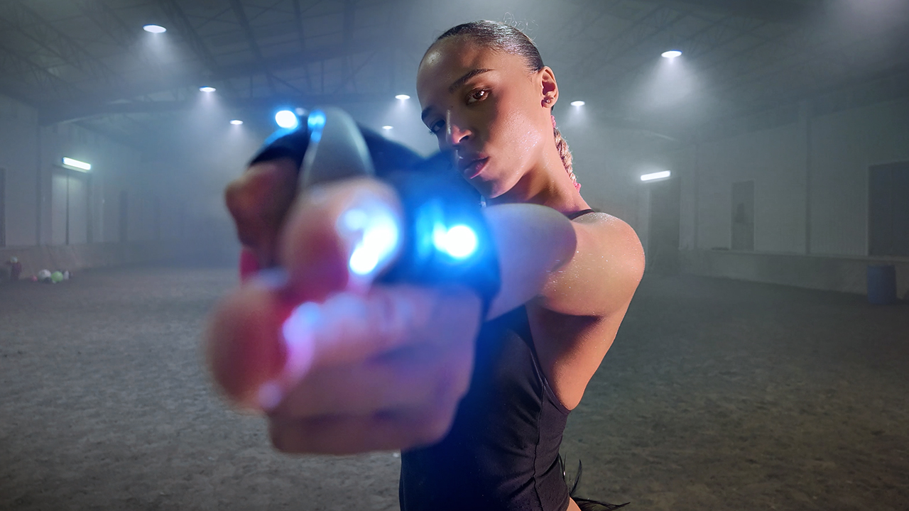 Zsela reaches toward the camera in a blue-lit gym