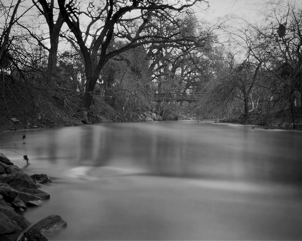 Serene long exposure of river flowing through bare trees with soft water movement and misty atmospheric quality