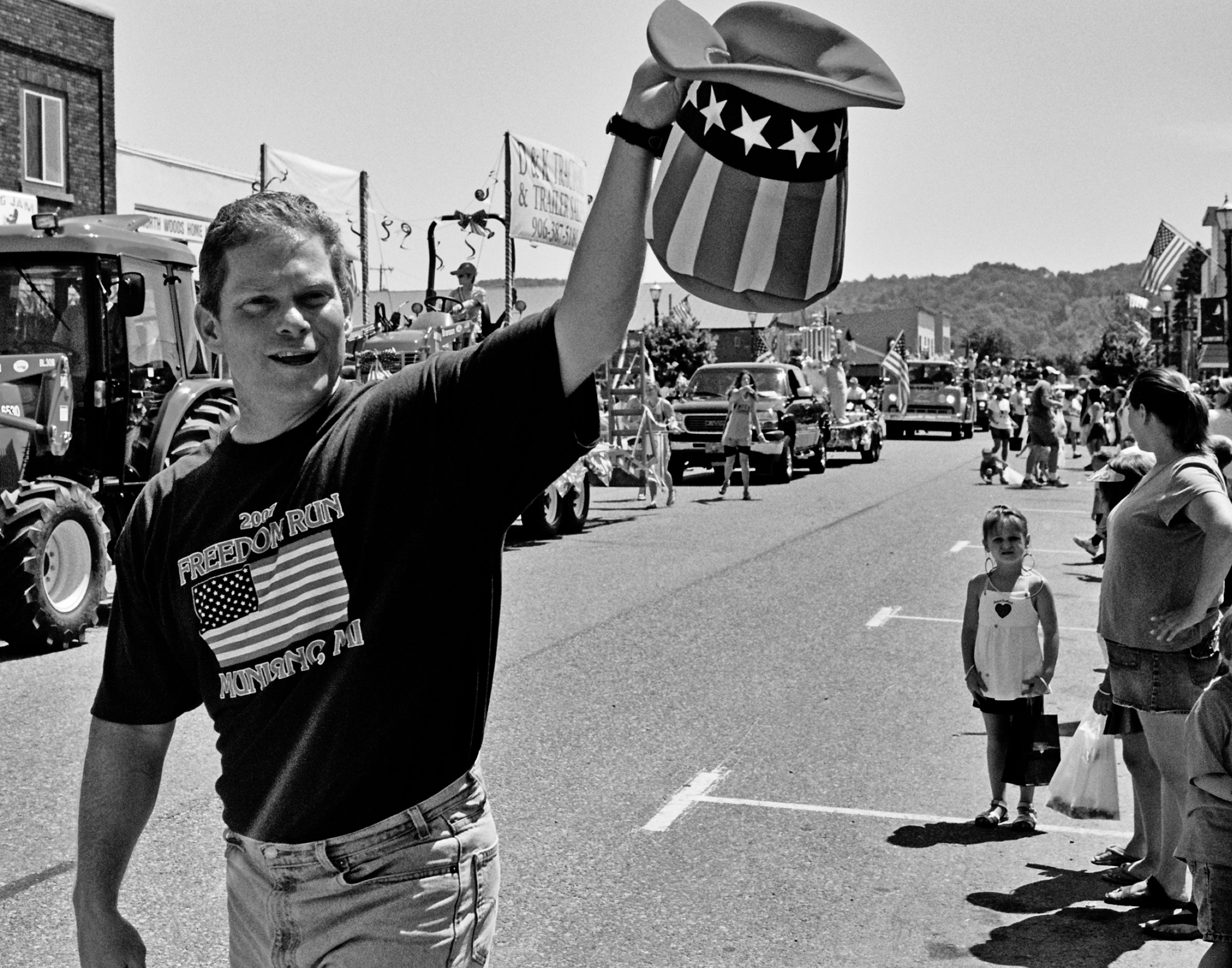 Man in Freedom Run Munising shirt waving patriotic Uncle Sam hat at Fourth of July parade
