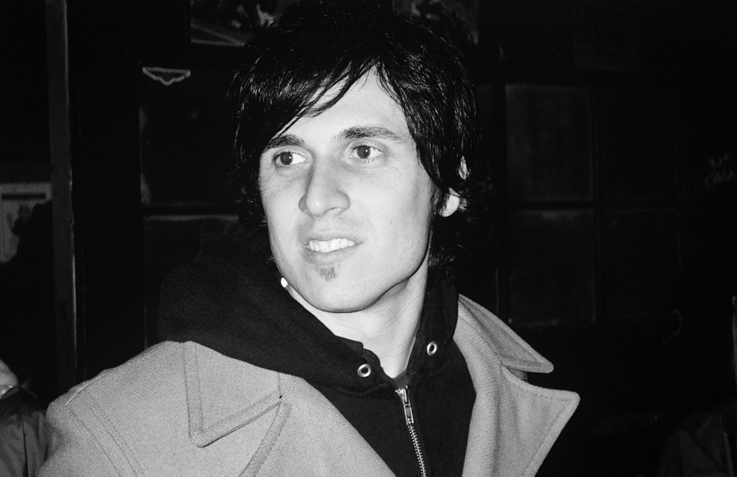 Close-up portrait of man with dark shaggy hair wearing layered jacket in candid moment