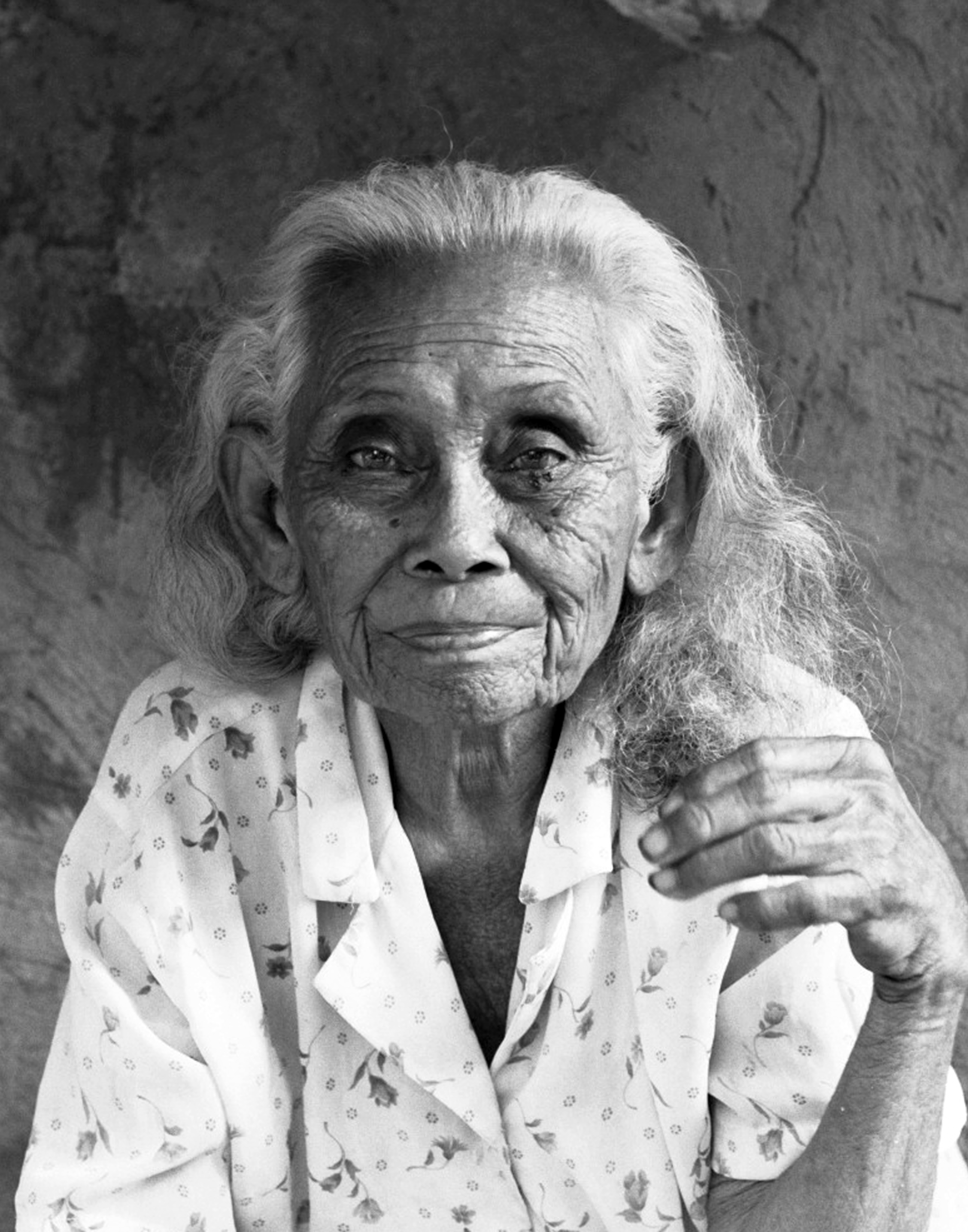 Portrait of elderly Filipino woman with white hair wearing patterned white jacket smiling gently at camera