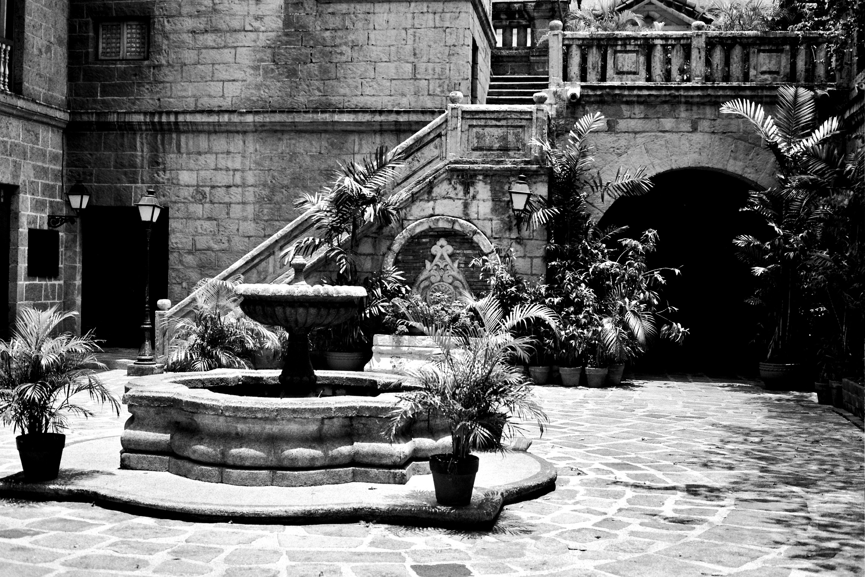 Spanish colonial courtyard with arched gateway stone fountain palm trees and weathered architectural details