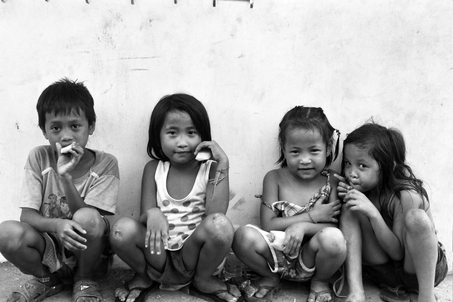 Four young Filipino children sitting together against white wall showing various expressions and poses