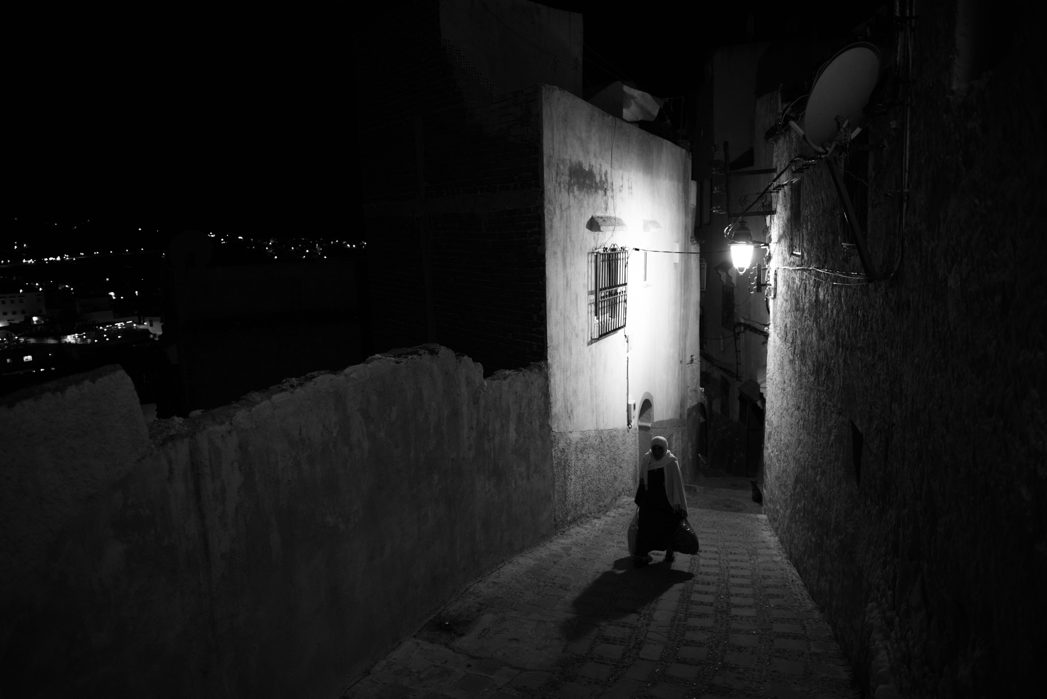Figure walking through lit Moroccan medina alley at night