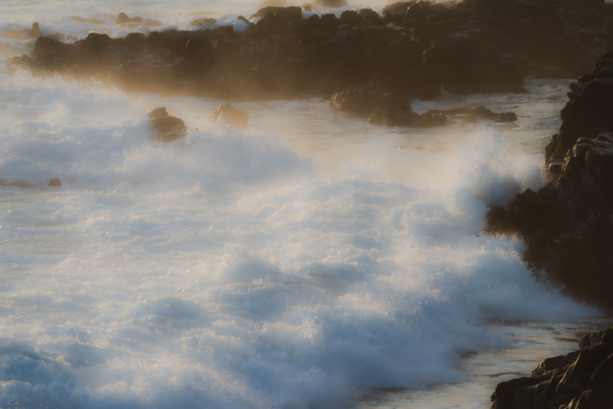Ocean waves crashing with golden mist on rocks
