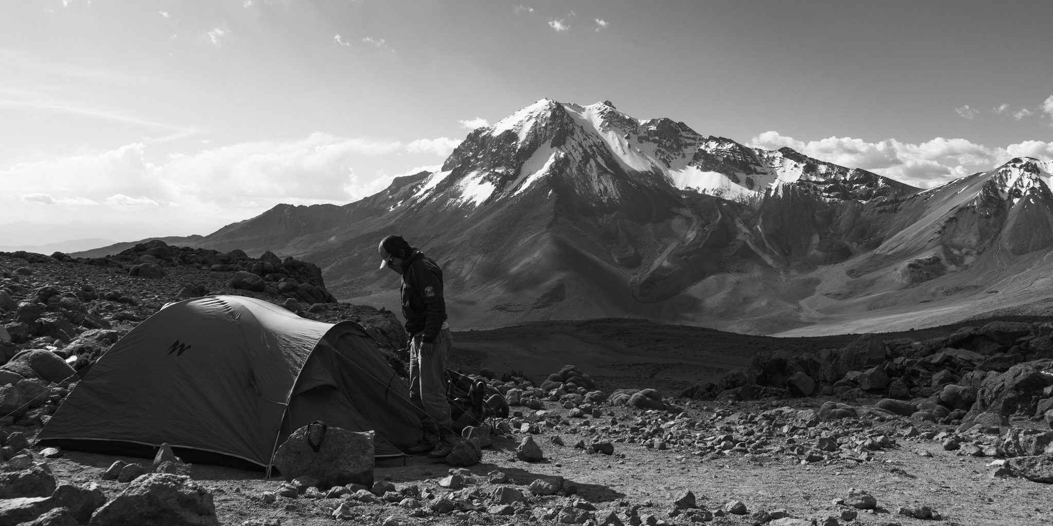 Hiker standing by tent with snow-capped volcano backdrop