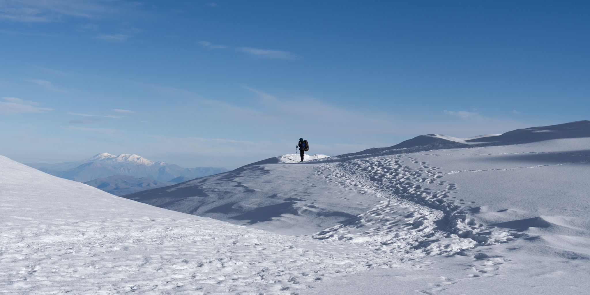 Person hiking on snowy mountain with footprints trail