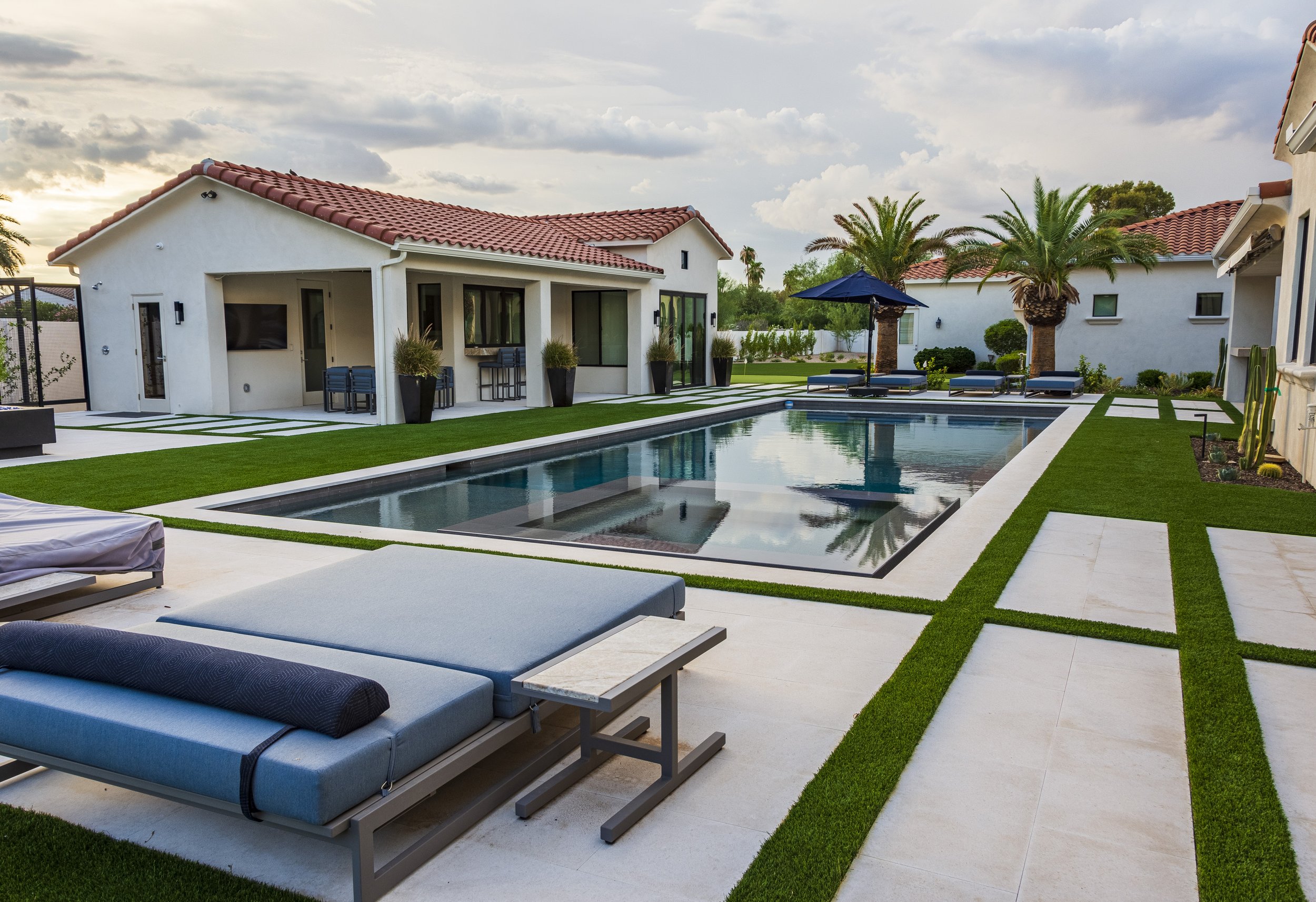 Resort-style pool with lounge chairs, turf, and casita at dusk