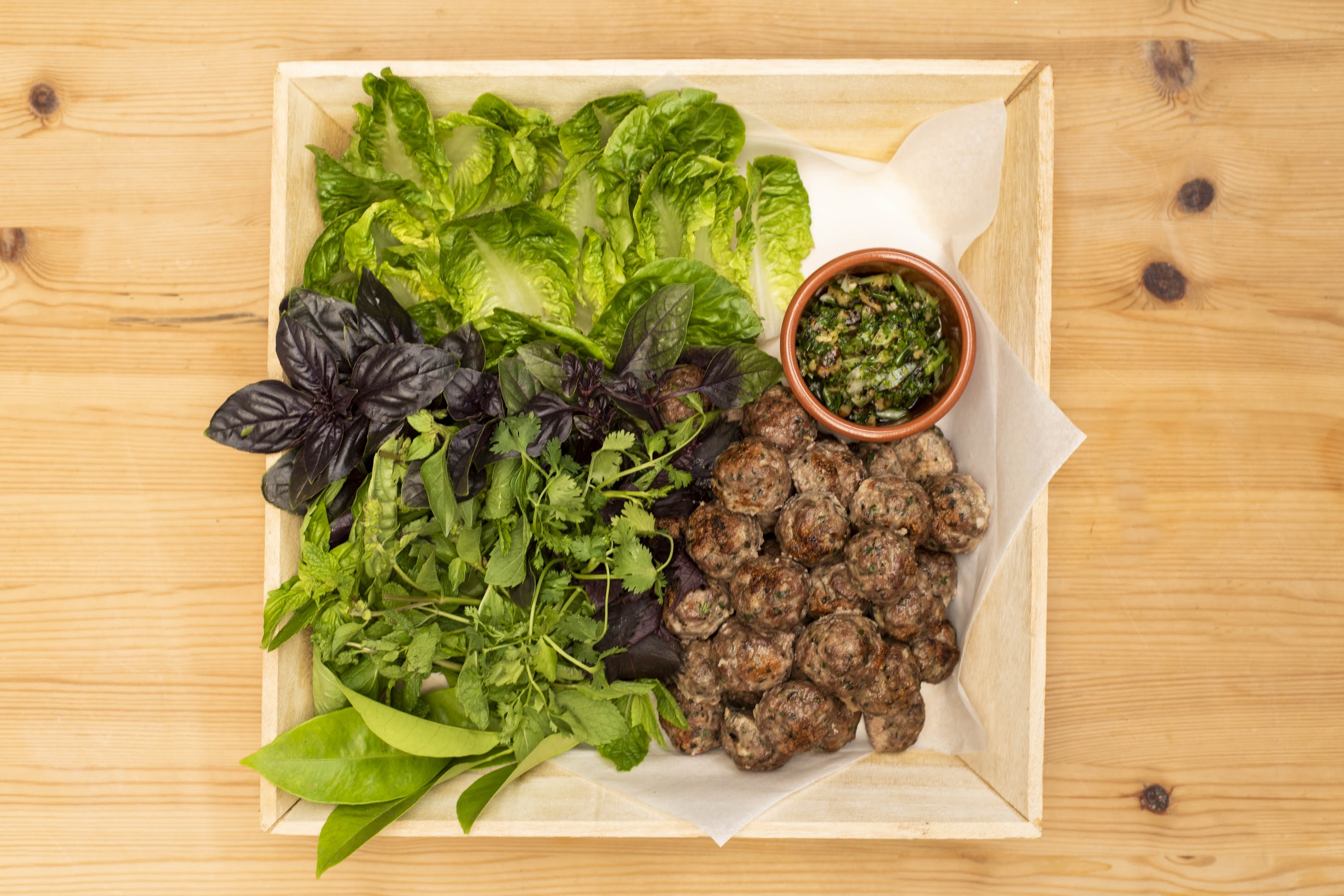 Catering tray of grilled meatballs with fresh herbs, romaine, and herb sauce