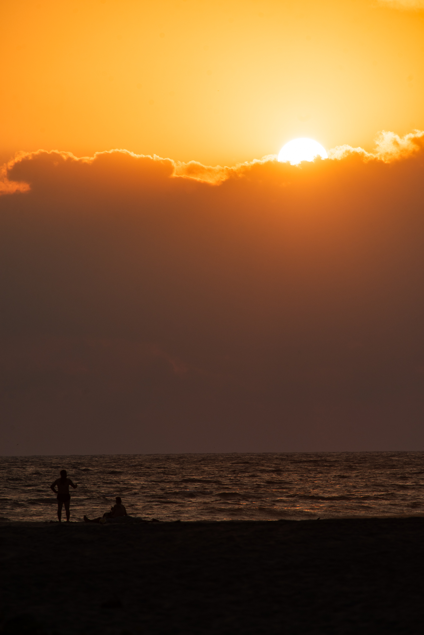 Silhouettes of people on beach with bright orange sunset