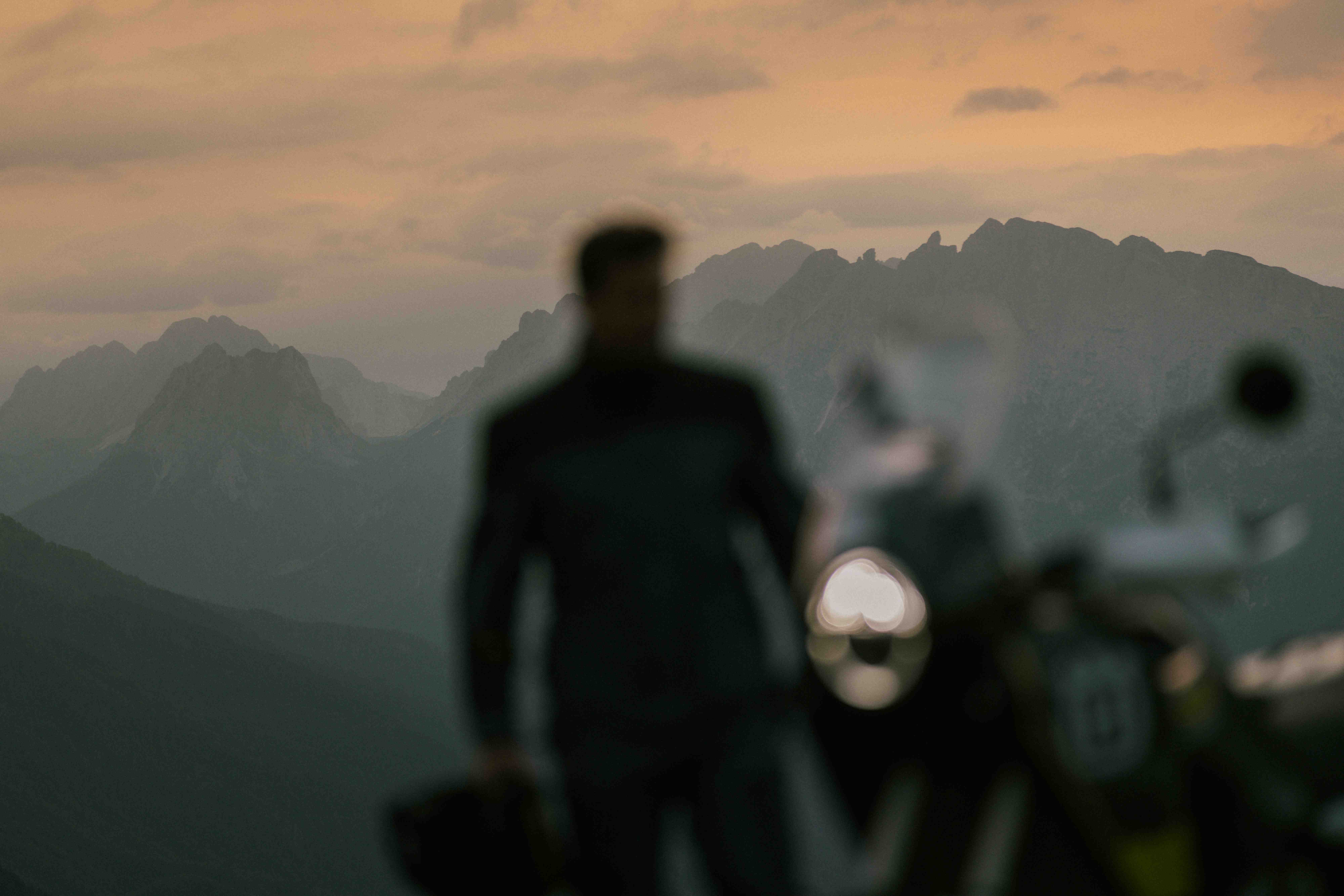 Soft atmospheric silhouette of a rider standing before a motorcycle at mountain sunset