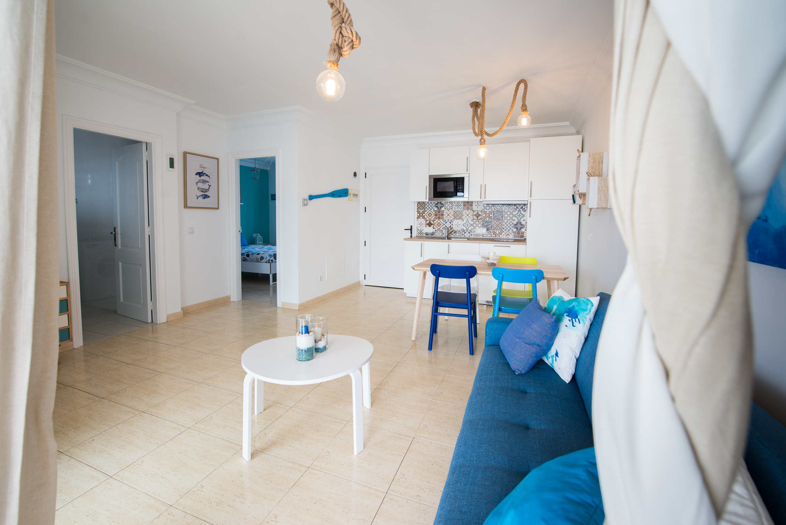 Open-plan living room with blue sofa, dining area, and kitchen with rope chandelier