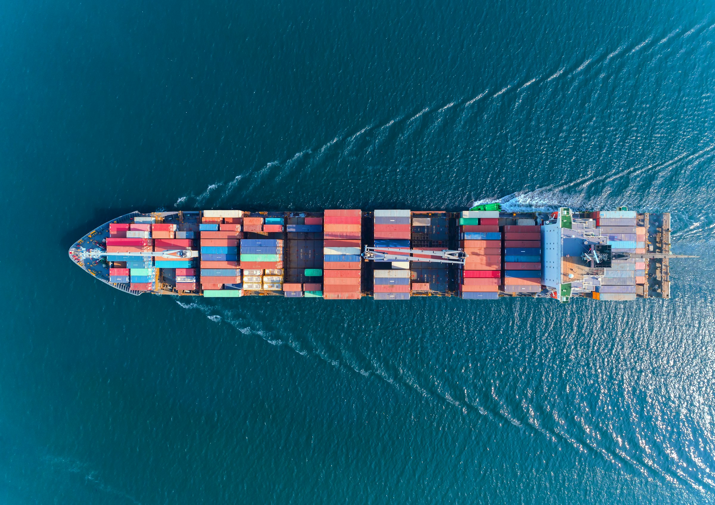 Aerial view of cargo ship loaded with colorful containers on turquoise ocean