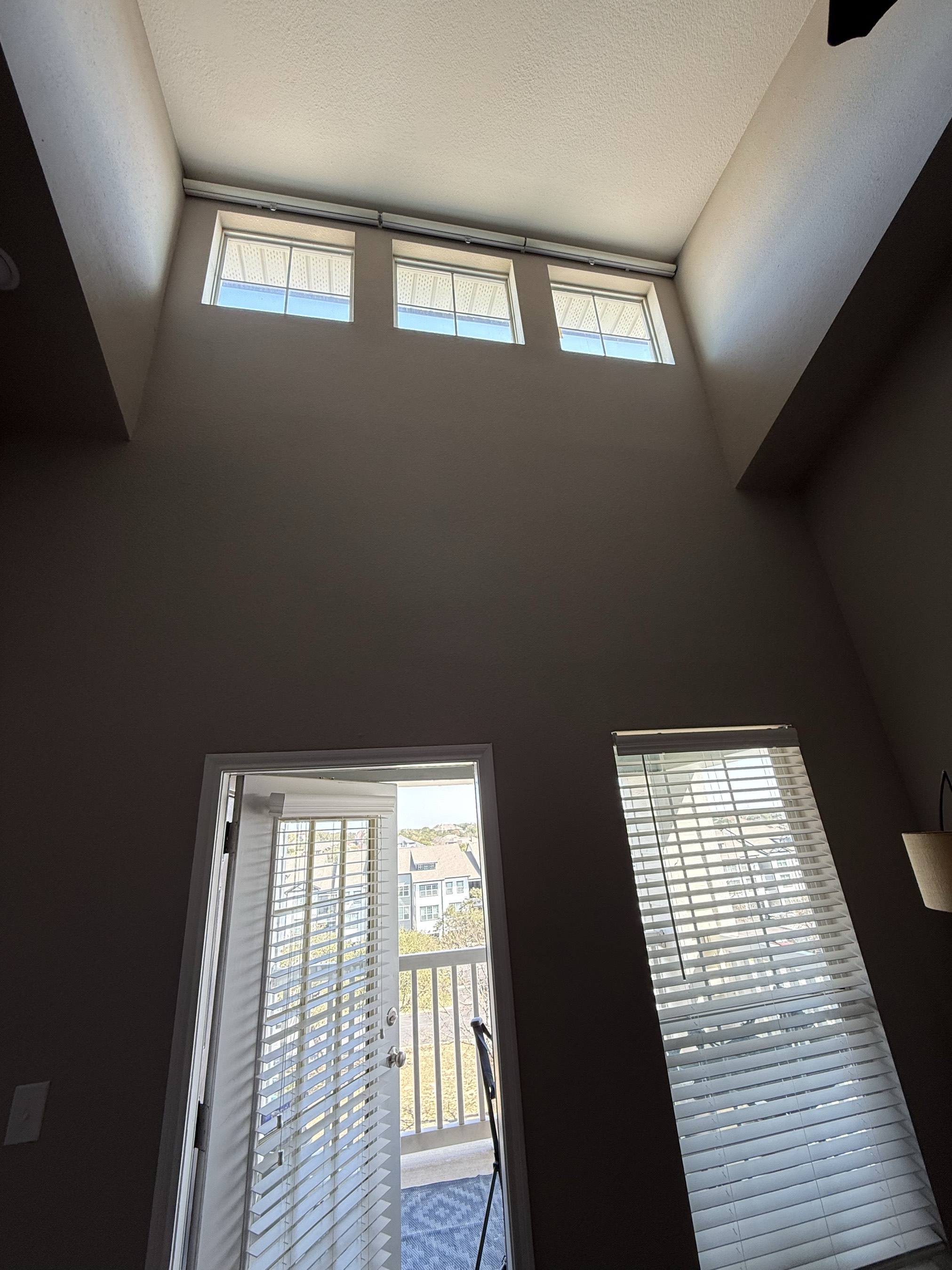 Two-story room with blinds on high windows and doors