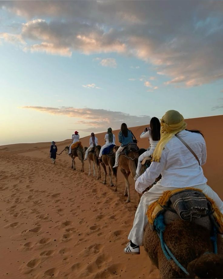 Group of tourists riding camels during golden hour sunset across the dunes