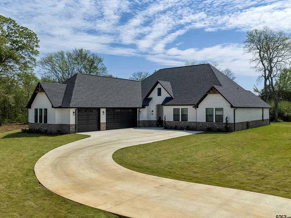 Craftsman exterior with curved driveway, dark roof, and wooded lot