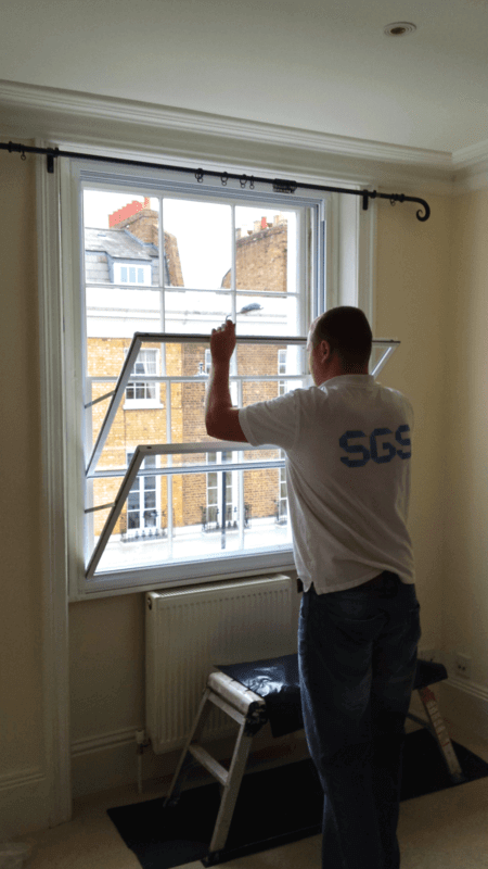 Professional installer fitting secondary glazing panel to Victorian sash window in London Mayfair townhouse