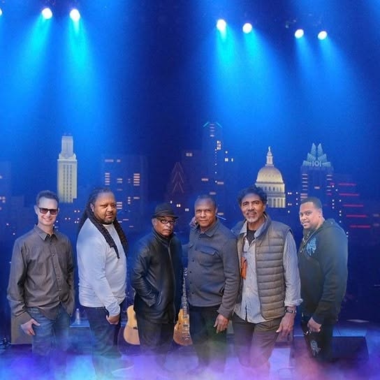 Alchemy Band — all six members on stage under dramatic blue lighting with a city skyline backdrop