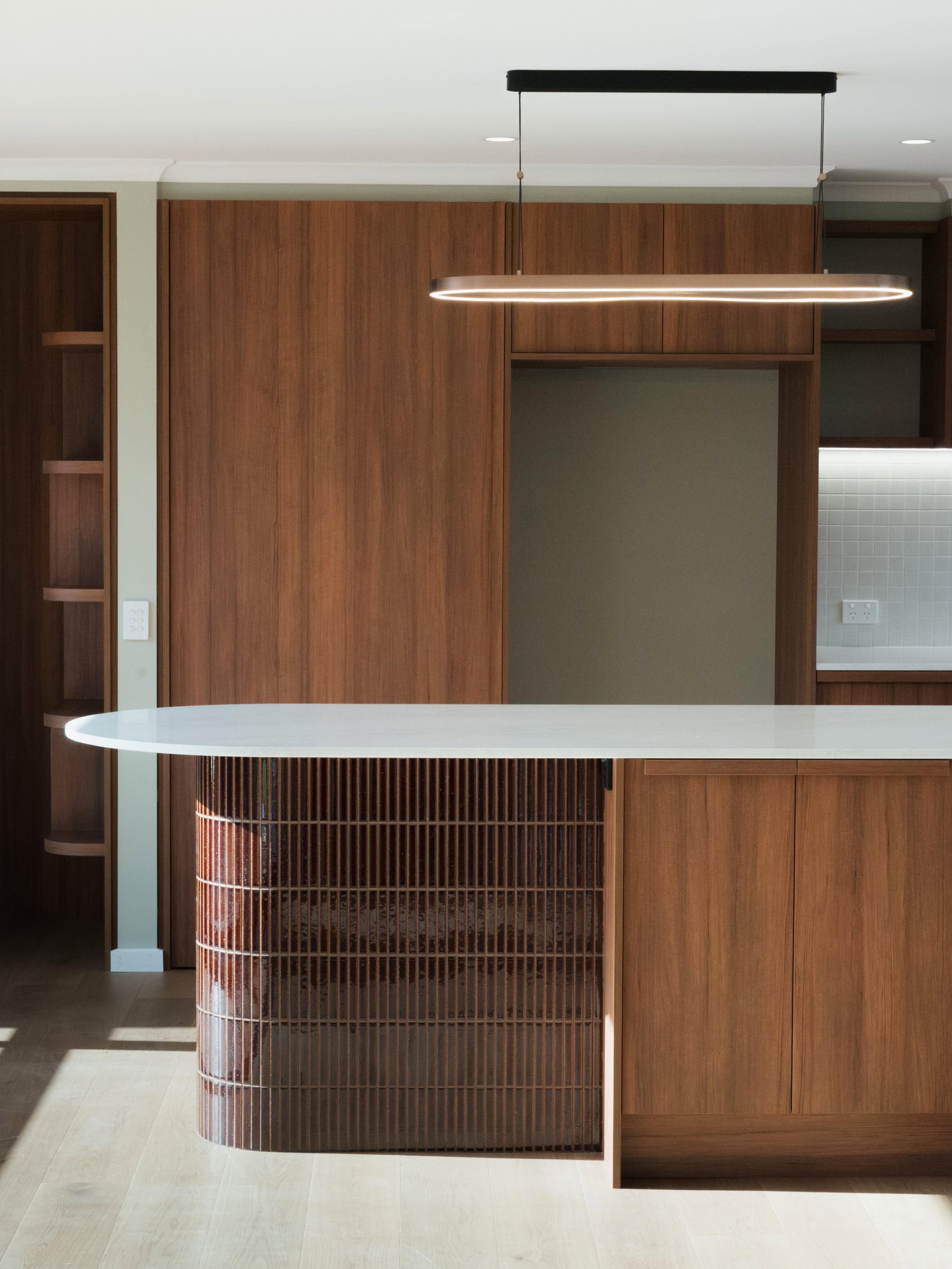 Curved timber kitchen island with pendant lighting and built-in joinery