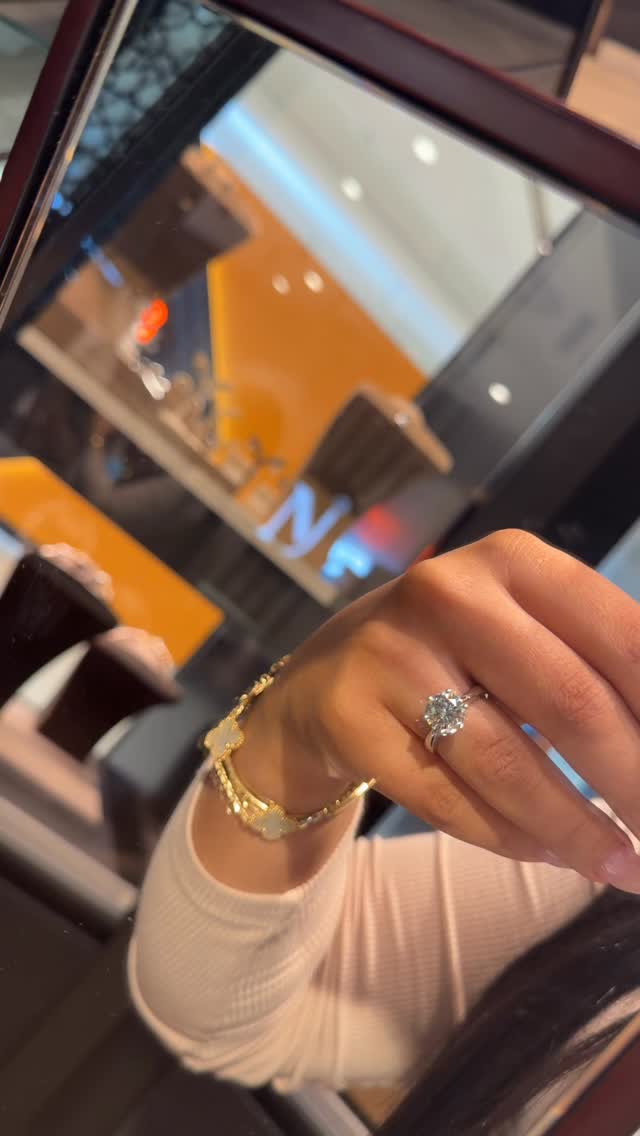 Solitaire diamond ring with gold bracelet and store signage reflected in mirror