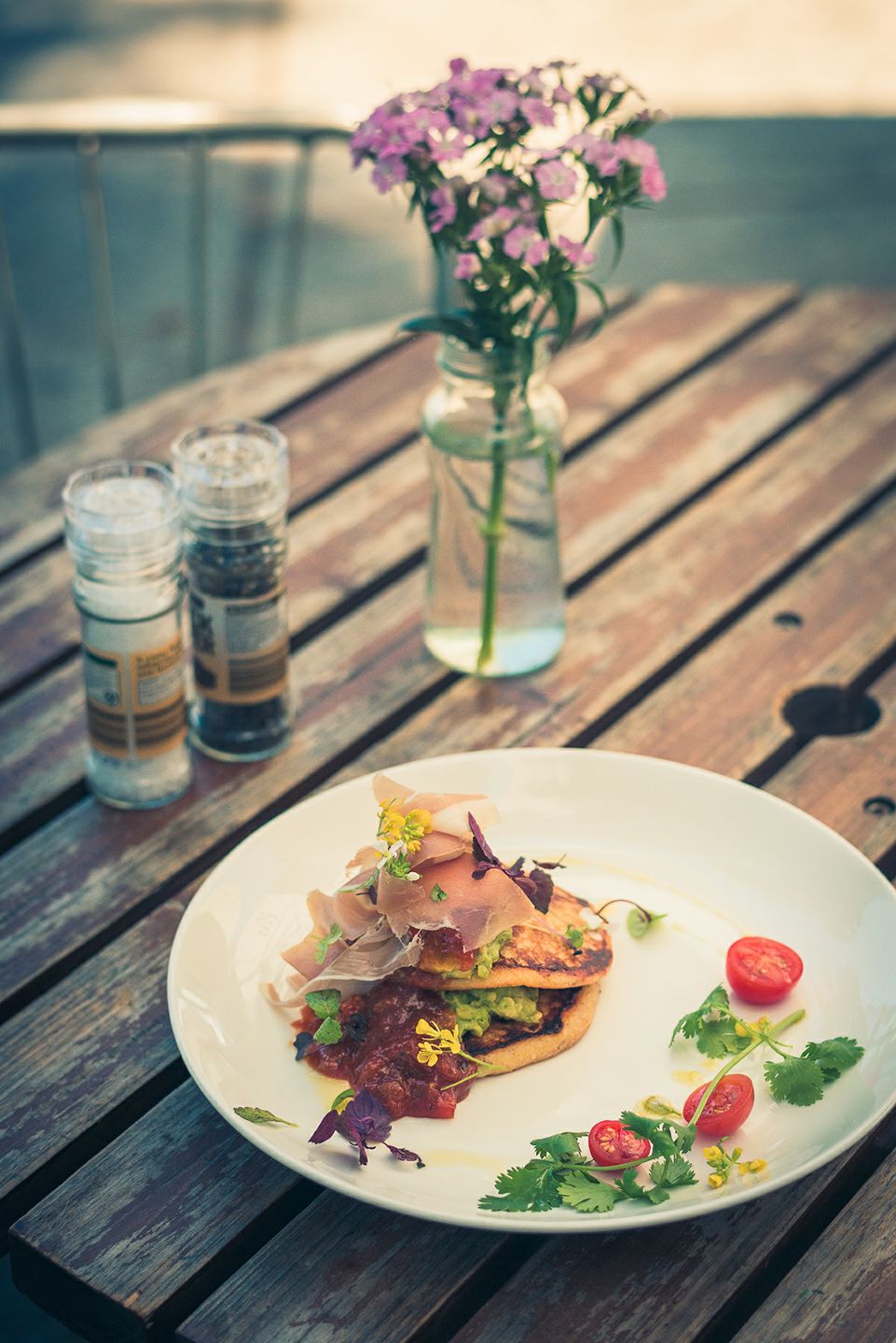 Beautifully plated brunch dish with corn fritters, prosciutto, guacamole and cherry tomatoes on a white plate at Monday Morning Cafe