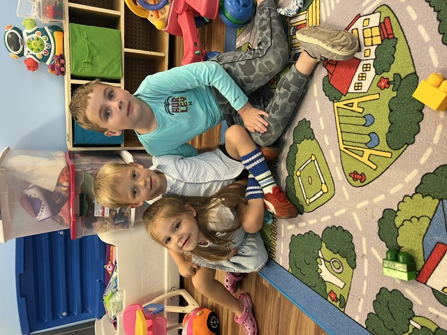 Three young children sitting together on a rug in the church nursery playroom