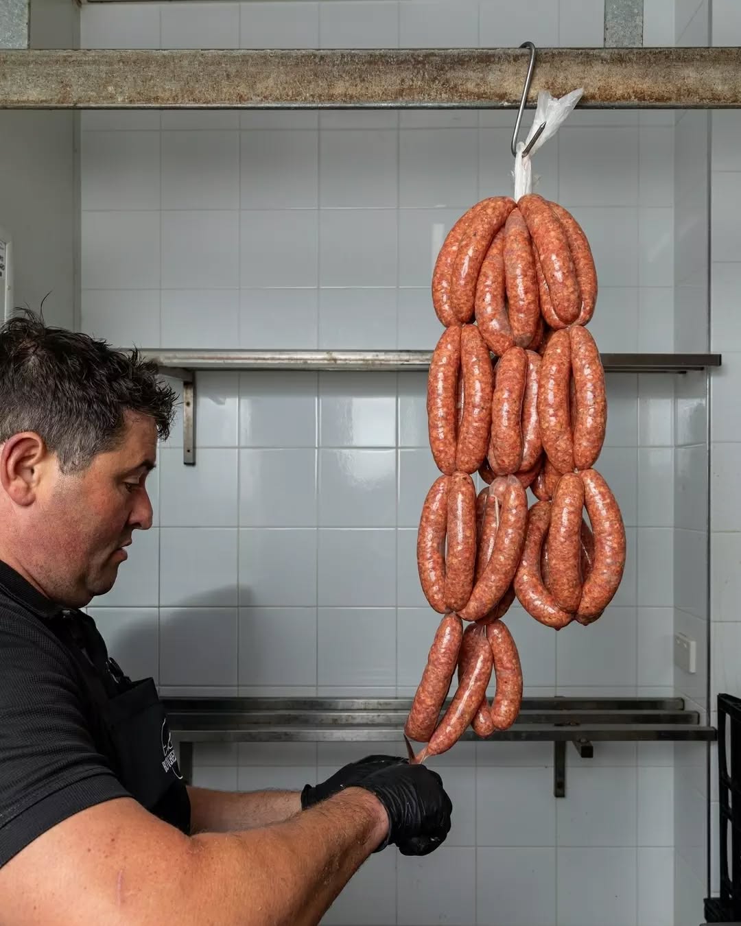 Butcher hanging freshly made sausage links in the preparation area