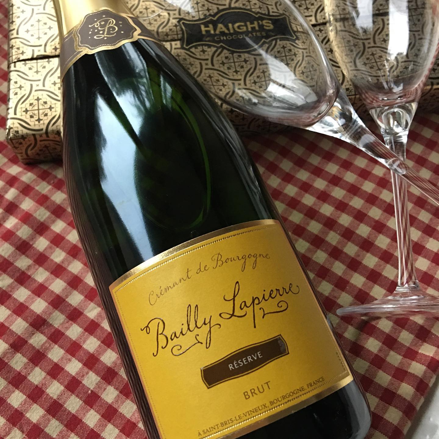 A bottle of sparkling wine lying next to two empty glasses on a red and white gingham cloth