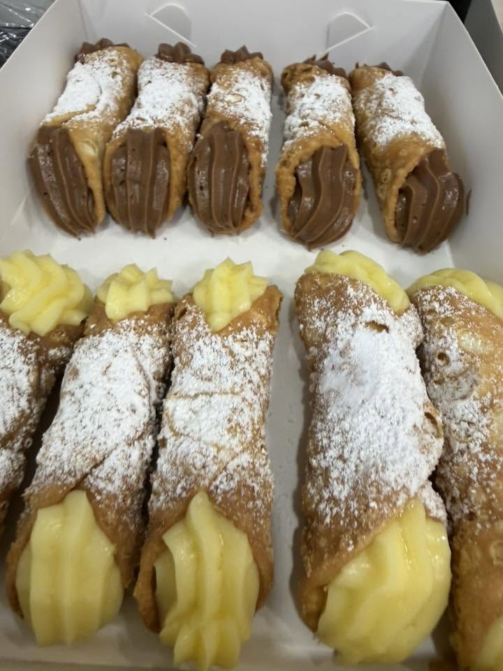 Pistachio-coated ricotta cannoli on a white plate dusted with icing sugar