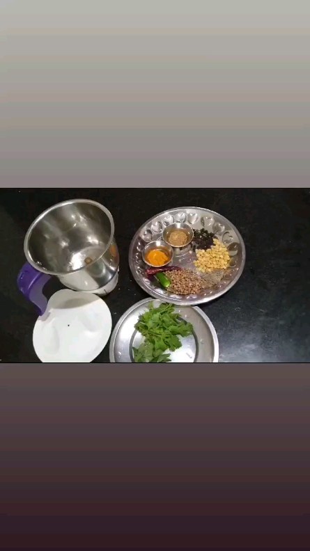 Indian spices on a steel tray with coriander leaves and a grinder
