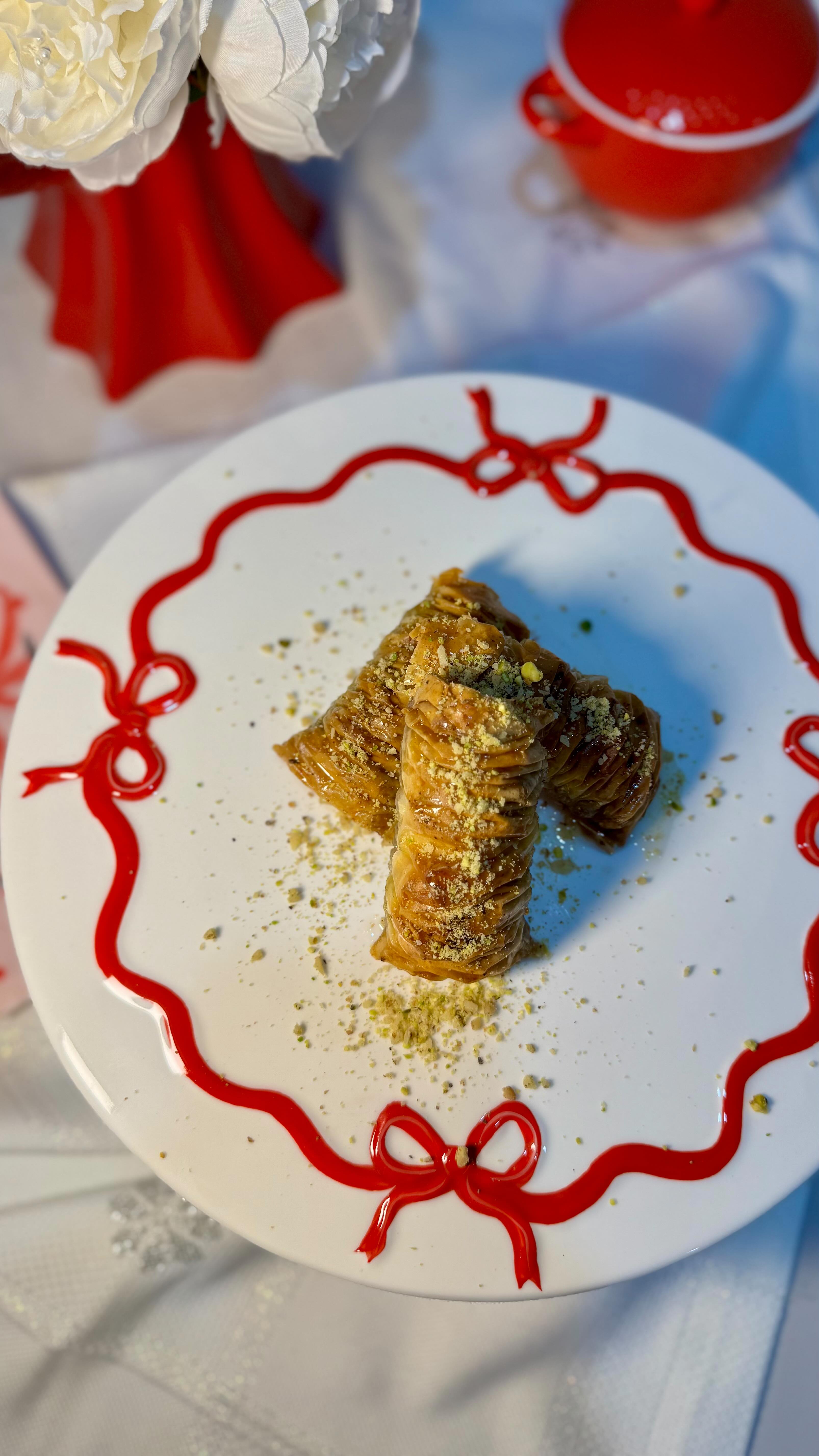 Golden, hand-rolled baklava dusted with crushed pistachio, plated and drizzled with syrup