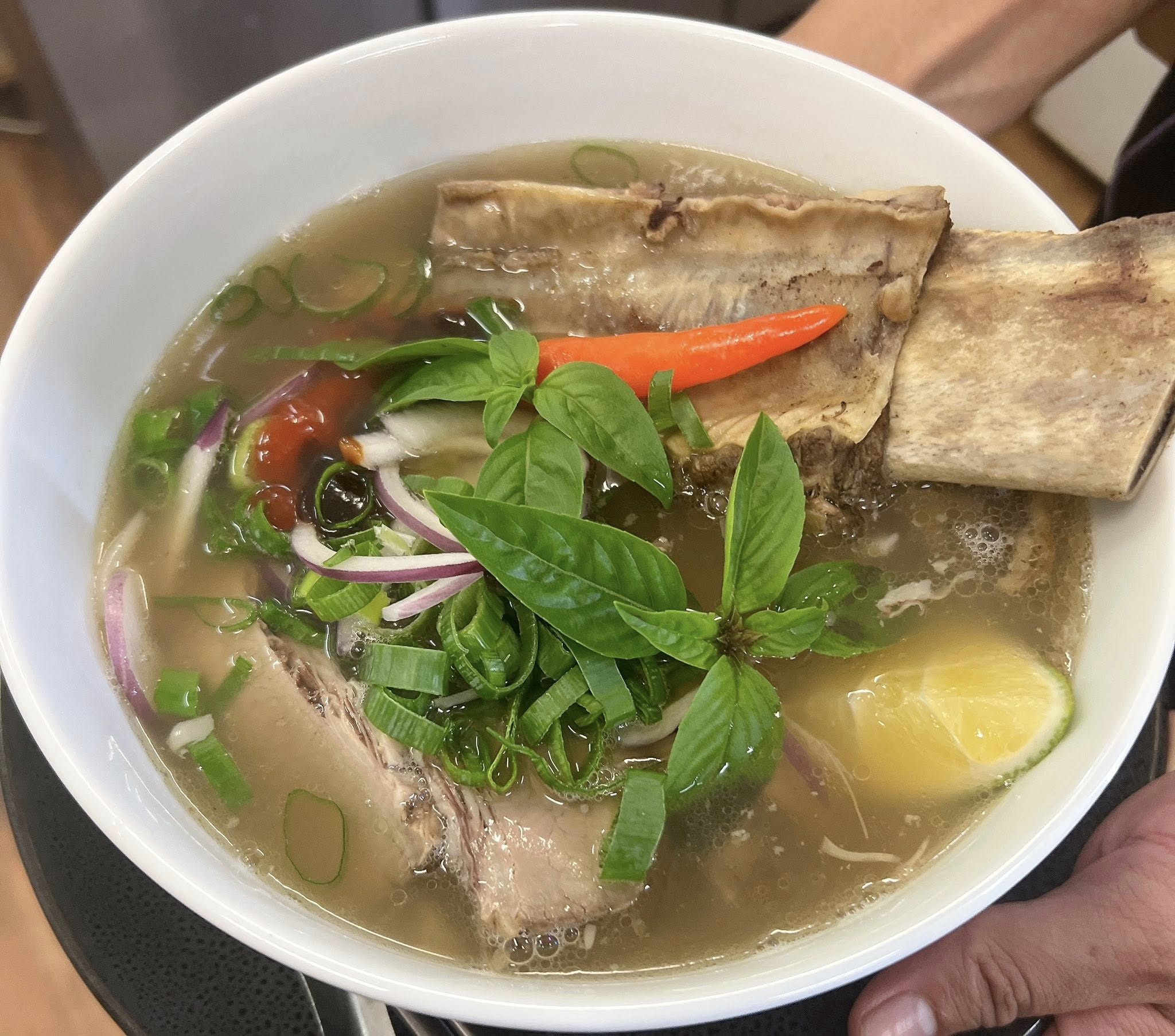 Bowl of Vietnamese pho with beef, bone broth, fresh herbs, chilli, red onion and lemon in a white bowl