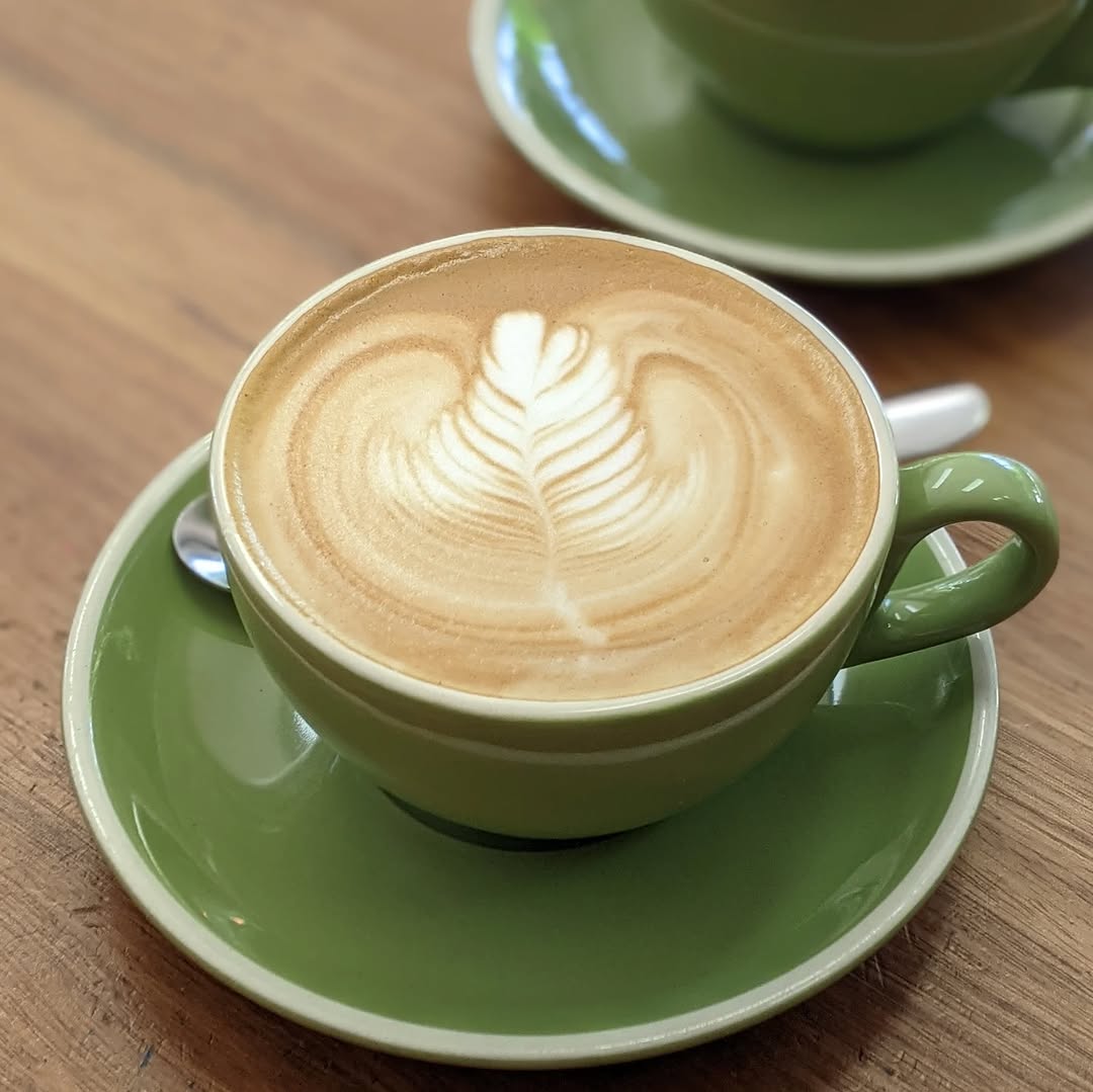 Cafe latte with leaf-pattern latte art in a green cup