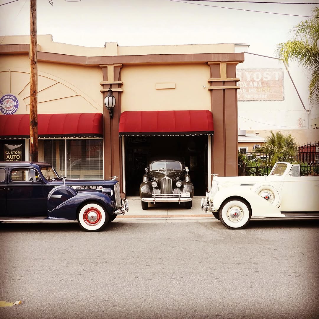 Three classic vintage automobiles parked outside a custom auto service shop