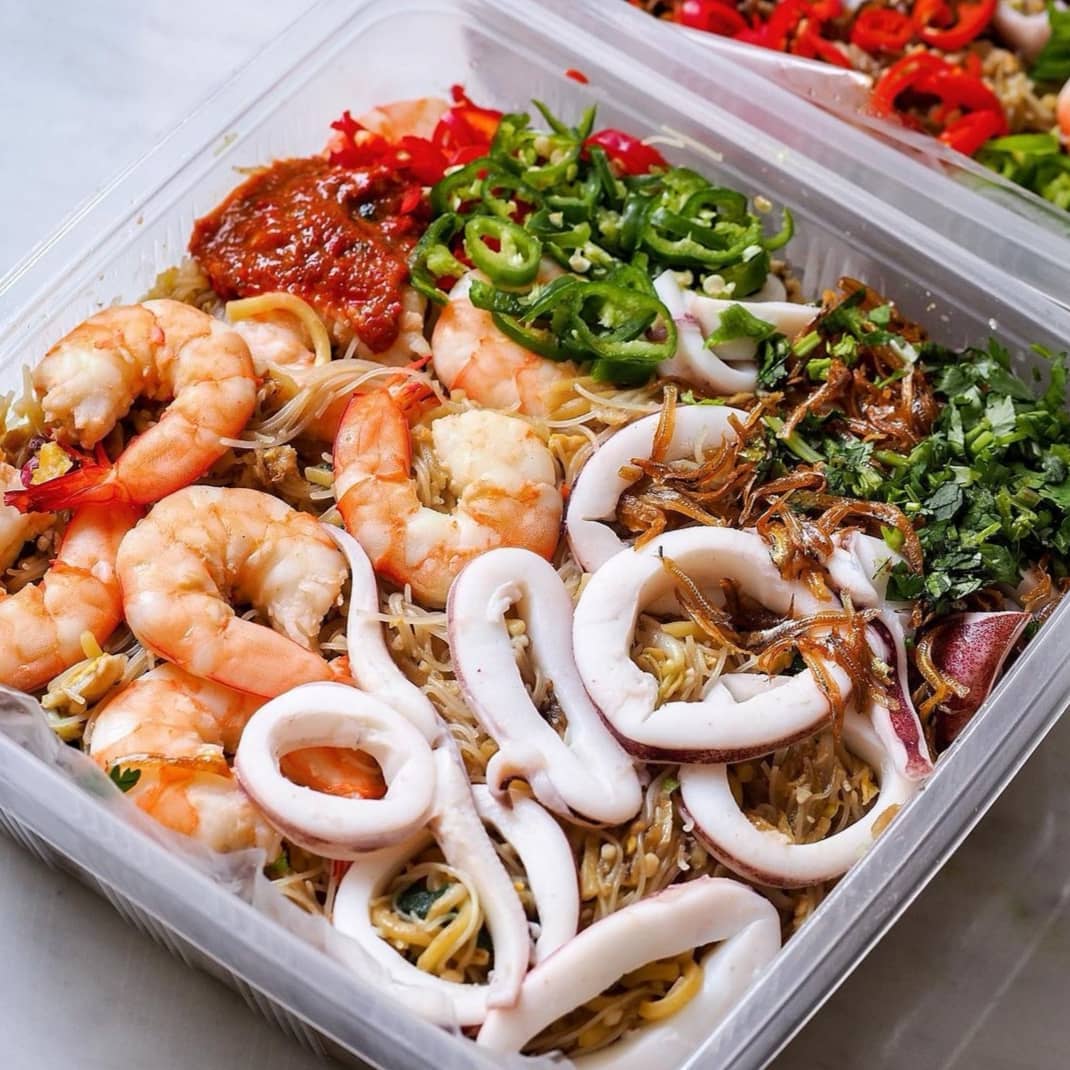 Close-up of Hokkien Mee takeaway platter with prawns, squid rings, sambal and green chilli