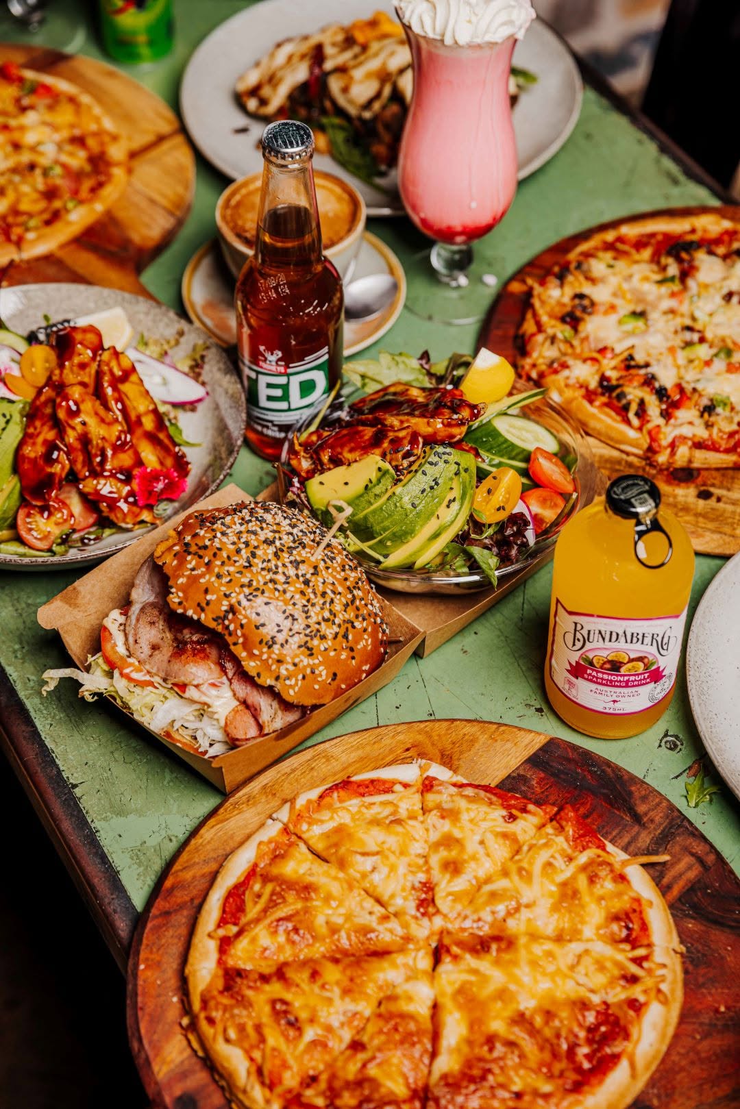 Spread of food and drinks at Nunzios Garage Cafe including pizza, burgers and salads on a green table